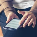 Close-up of adult using smartphone indoors, browsing web with focus on screen.